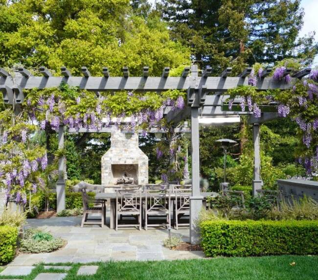 outdoor dining area beneath a wooden pergola, adorned with flowering wisteria vines